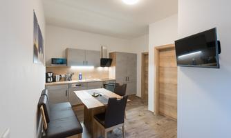 A modern kitchen with a dining table and chairs. The walls are bright, and the furniture is simple and functional.