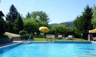 A clear pool in a green garden with sun umbrellas. In the background, there are trees and a blue sky.