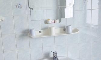 A simple bathroom with a sink, a mirror, and minimal decoration. The walls are brightly tiled and give a clean impression.