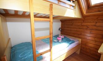A cozy bedroom with a wooden bunk bed. On the lower bed, there is a blanket and a toy.