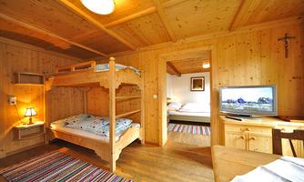 A cosy room with wooden paneling, a bunk bed, and a television. In the background, another bed and a carpet are visible.