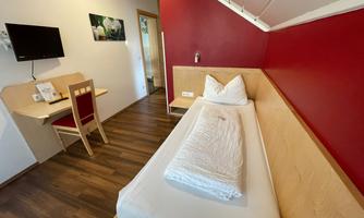 A simple room with a single bed and a red wall. The room features a desk and a television.