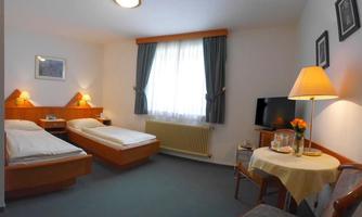 A simple room with two single beds, a table, and a television. Large windows let in plenty of daylight and the decor is cozy.