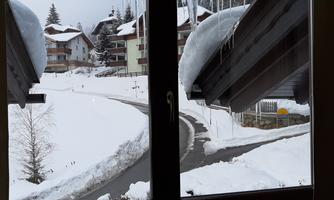 A snowy winter view through the window. The snow-covered roofs and trees create a calm, alpine atmosphere.