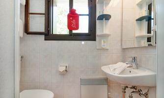 A bathroom with a sink, a toilet, and a window. The walls are brightly tiled and there is a towel rack as well as shelves.