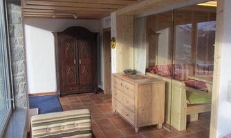 A cozy room with wooden furniture and a large window. Next to a stone wall stands a beautiful wardrobe.