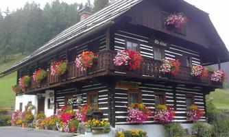 A beautiful wooden house with colorful flower boxes and a green garden. The surroundings are green and hilly.