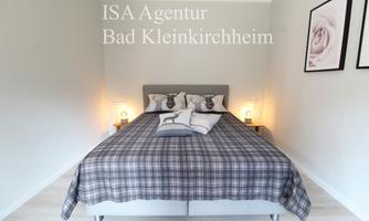 A cozy bedroom with a large bed and bright wall lights. The walls are kept neutral and there are decorative pictures.