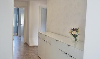 A modern hallway with a bright floor and a long white wardrobe. There is a bouquet of flowers on a shelf.