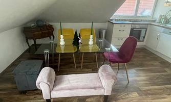 A cozy dining area in the attic with a glass table and colorful chairs. The decor is modern and inviting, with wooden flooring and stylish accessories.