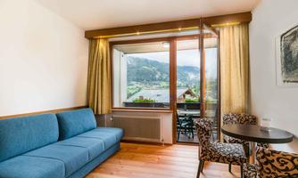 A cozy living area with a blue sofa and a round table. The window offers a view of the mountains and nature.