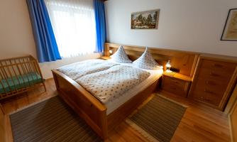 A cozy bedroom with a double bed and two pillows. There is a window area with blue curtains and a wardrobe.