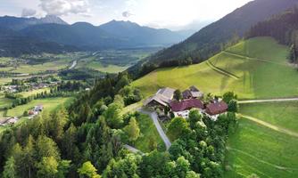 A picturesque landscape with gentle hills and green meadows. In the foreground stands a cozy farmhouse, surrounded by trees and mountains in the background.