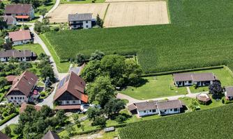 A beautifully laid-out village with several houses surrounded by fields and plants. The landscape is green and peaceful.