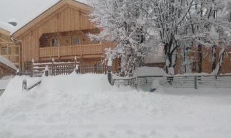 A wooden house in a snowy landscape. The snow covers the garden and the surroundings.