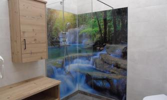 A modern bathroom with a glass shower and a wooden cabinet. The wall is decorated with a vibrant waterfall motif.