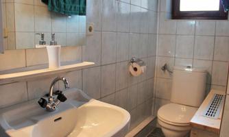 A bright bathroom with white tiles. There is a sink, a toilet, and a towel holder.