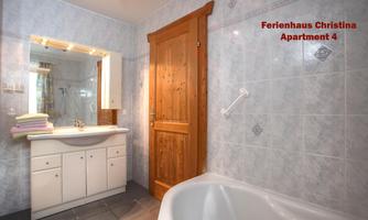 A modern bathroom with a bathtub and a sink. The walls are brightly tiled and there are wooden details on the door.