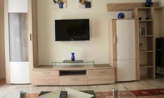 A modern living room with a television on the wall and a stylish coffee table. The furniture is made of light wood and there are decorative elements like vases and pictures.