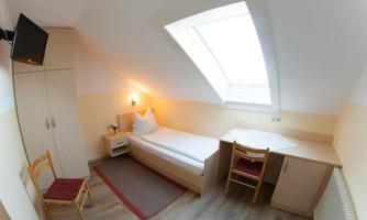 A cozy room with a single bed and a desk. The skylight allows for plenty of daylight.