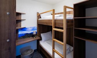 A modern room with a wooden loft bed and a desk. There are shelves and a television in the room.