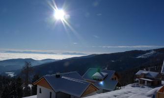 A winter landscape with snow-covered houses. The sun shines over the mountains and a layer of clouds.