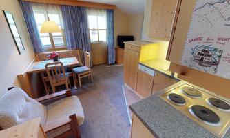 A cozy room with wooden furniture and a small dining area. The kitchen is well-equipped with a stove and offers plenty of daylight.