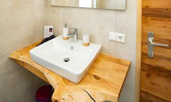 A modern sink on a wooden base in a bathroom. In the background, a mirror and a wooden door are visible.