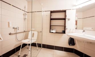 A barrier-free bathroom with a shower cabin and grab bars. There is a shower chair and a modern sink arrangement.