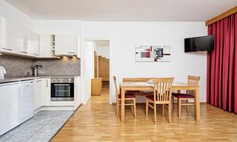 A modern kitchen with a dining table and chairs. The room has a friendly, open layout and large windows.