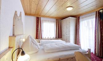 A cozy bedroom with wooden paneling and two beds. The windows are bright and offer plenty of daylight.