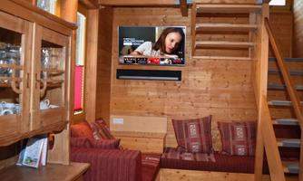 A cozy living space with wooden walls and a television on the wall. There is a sofa with cushions and a staircase leading upstairs.