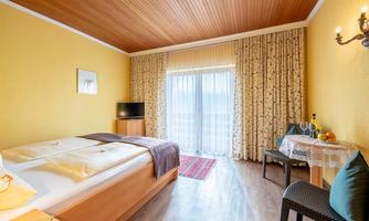 A bright room with two beds and a small table. Large windows let in a lot of light, and the walls are painted in warm shades of yellow.