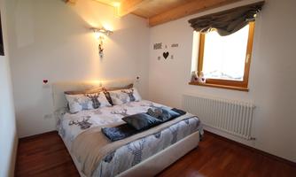A cozy bedroom with a large bed and wooden ceiling. The window lets in plenty of daylight and creates a warm atmosphere.