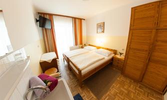 A bright room with two beds, a television, and a wardrobe. In the background, there are windows with curtains and a cozy atmosphere.