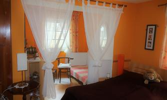 A cozy bedroom with orange walls and bright light. There is a large bed, a chair, and a small table.