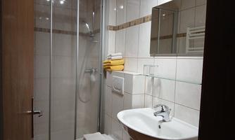 A modern bathroom with a shower and a sink. Towels in yellow and white are neatly folded.