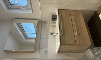 A modern bathroom with a wood vanity and a large mirror. The room has light walls and a window that lets in daylight.