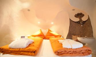 A cozy bedroom with orange pillows and blankets. The walls are gently curved and the lighting creates an inviting atmosphere.