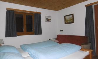 A cozy bedroom with a double bed and a red couch. The walls are decorated with pictures, and the window has curtains.