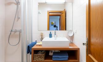 A modern bathroom with a sink on a wood infusion and a large mirror. In the background, a shower and an open door are visible.