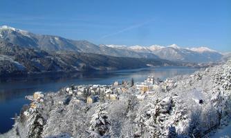A winter landscape with snow-covered mountains and a tranquil lake. In the foreground lies a picturesque village surrounded by frosty fir trees.
