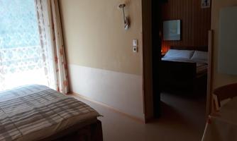 A simple hotel room with two beds. The room has a window overlooking a balcony and a warm atmosphere.
