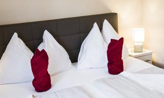 A cozy bedroom with a double bed and white pillows. A lamp is on the nightstand.