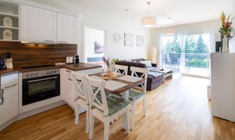 A modern kitchen with wooden details and an open living area. The room has large windows that let in plenty of daylight.