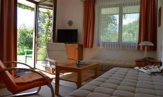 A bright living room with a large window and a view of the garden. There is a television, a table, and comfortable seating.
