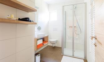 A modern bathroom with a shower and a bright, inviting atmosphere. Shelves with towels and toiletries complement the stylish design.