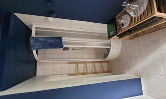 A modern bathroom with a shower cabin and blue walls. There is a wooden shelf and some decorative elements.