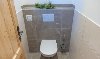 A modern bathroom with a white toilet and elegant gray tiles. At the top of the wall, a small plant is decorated.