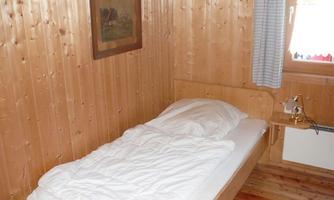 A simple room with a single bed and wooden-panelled walls. There is a window with curtains and a painting on the wall.